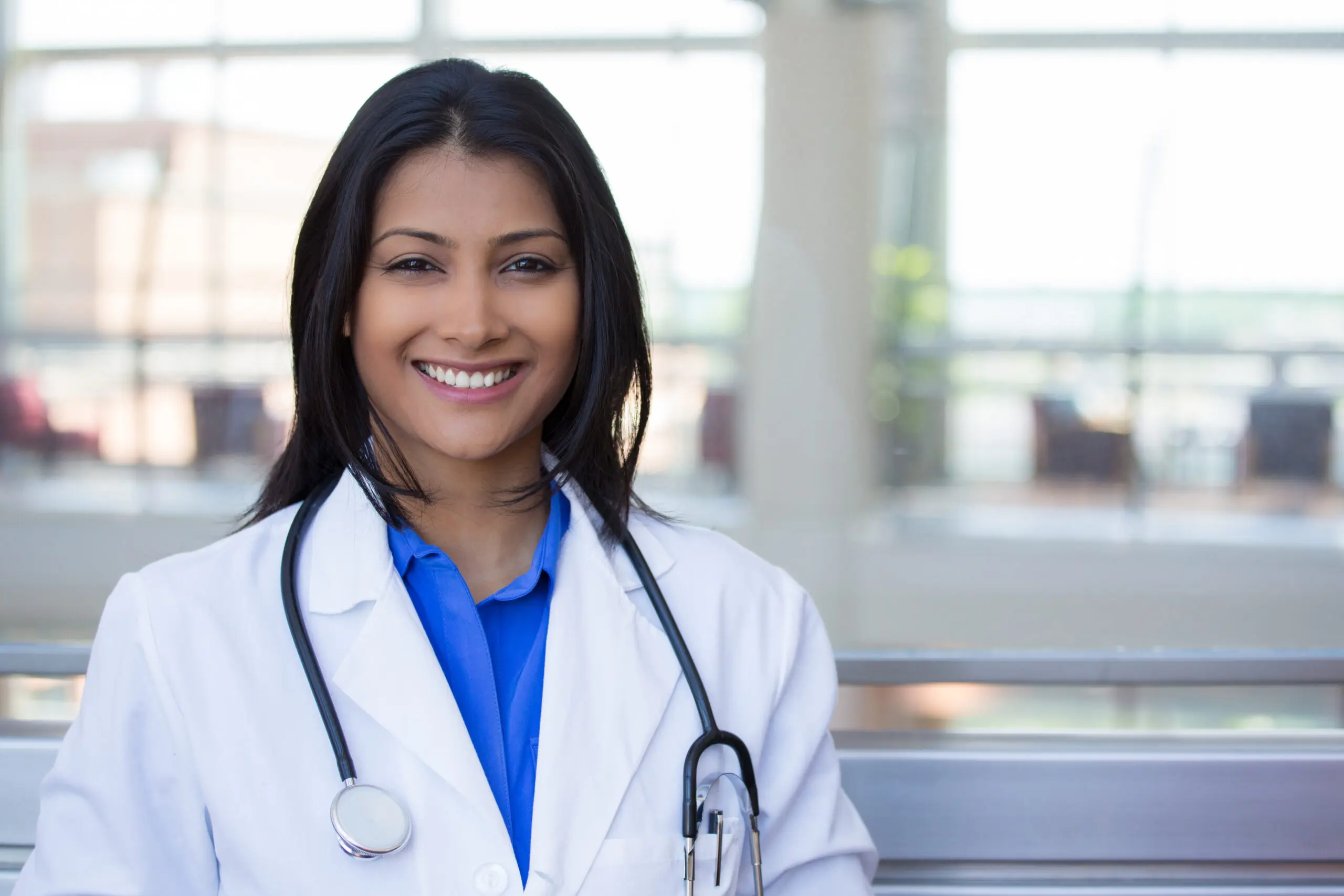 Female doctor smiling in a healthcare setting, representing the efficiency improvements offered by Dragon Medical One version 2024.3 for medical professionals.